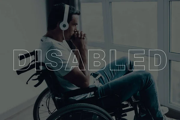 Disabled Man in a Wheelchair. Man Sits in Front of Window. Man Looks into Window. Man Listening Music on Headphones. Music on Mobile Phone. Man is Praying. Man Located in the Living Room.