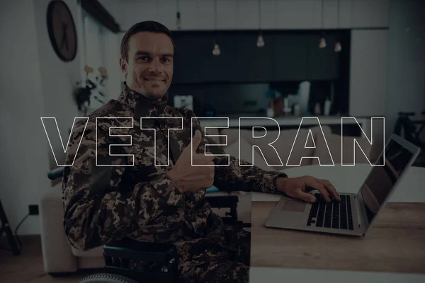 Military Veteran. Disabled Man in a Wheelchair. Man Sitting at Table. Man Using s Laptop. Man is Soldier. Soldier in Military Uniform. Man Showing OK Sign. Man Smiling. Man Located in the Living Room.