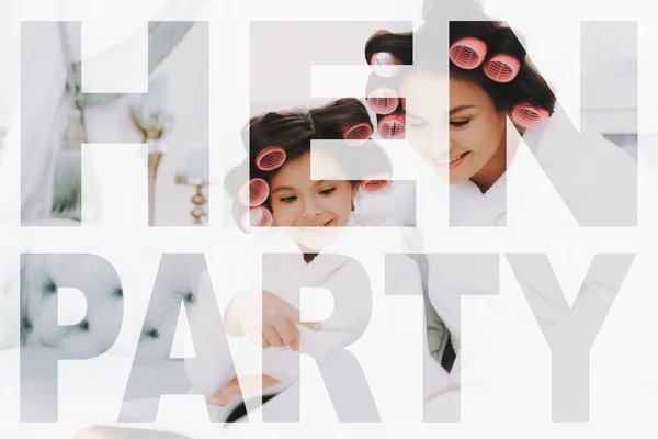 Family in White Bathrobes. Mother and Daughter sitting on the Couch. Women have Curlers in their Hair. Mother and Daughter Have Fun. Child is Flipping through the Magazine. Cropped Photo.