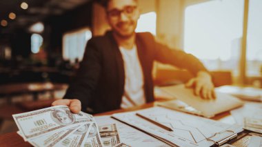 İş adamı elinde dolar maaş closeup. Takım elbise giymiş masada oturan bulanık metin yazarı portresi nakit tutar. Online iş ve uzak iş işçisi kavramı serbest