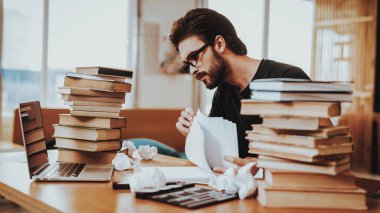 Genç metin yazar kapalı çalışma kavramı. Yakışıklı çalışkan serbest senaryo yazarı senarist iki büyük yığınlar yakınındaki masada oturan makale, roman yazma kitaplar, kağıt yapraklarının üzerinde oynamak.