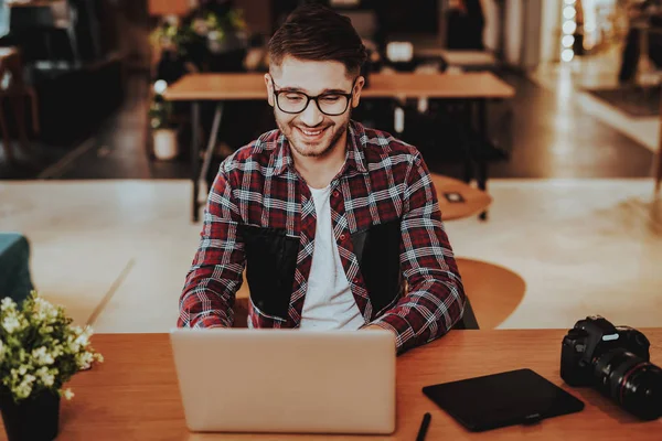 Dizüstü bilgisayarda çalışma Freelancer gülümseyen portresi. Yakışıklı beyaz Hipster grafik tasarımcı gözlük oturur becerikli alet ile masada kapalı giyer. Mesafe iş ve Freelancing kavramı
