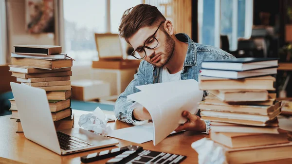 Pensive Freelance Text Writer Working at Desk. Handsome Hardworking Freelance Screenwriter Scenarist Sits Near Big Stacks of Books Writing Article, Novel, Play on Paper Sheets Looks Away