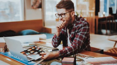Grafik tasarımcı tutar renk paleti esneme. İşyeri dizüstü bilgisayar ekranında projede çalışan seyir yorgun uykulu Genç beyaz Freelancer gözlüklü portresi oturur