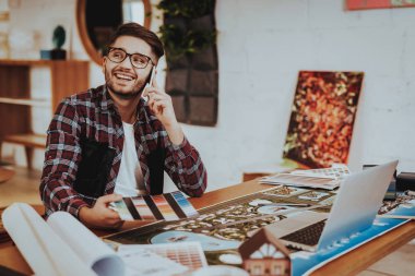 Illustrator telefon çalışmaları proje üzerinde konuşurken gülümsüyordu. Genç portresi sakallı hippi adam oturur dizüstü kullanarak işyerinde Smartphone tutan renk paleti. Yaratıcı grafik tasarım iş kavramı