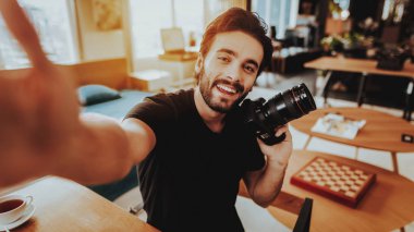 Gülümseyen adam olun İşyerinde çalışırken Selfie. Şık sakallı gülümseyen yakışıklı beyaz fotoğrafçı portre profesyonel fotoğraf el kapalı masada oturur tutar.