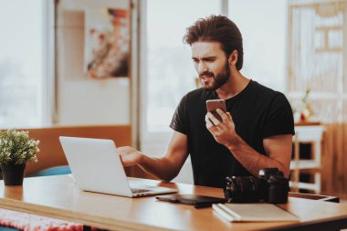 Gergin çocuk telefon dizüstü bilgisayarda uzaktan çalışıyor tutar. Kızgın şık serbest grafik tasarımcı portresi Smartphone oturur masada Frowns ekranında kapalı bakarken tutar. Mesafe iş kavramı