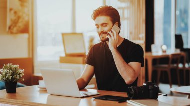 Mutlu adam görüşmeler telefon ve dizüstü bilgisayarda uzaktan çalışır. Gülümseyen mutlu beyaz Freelancer portresi kapalı masada oturur. İş mesafe ve iletişim kavramı Freelancing