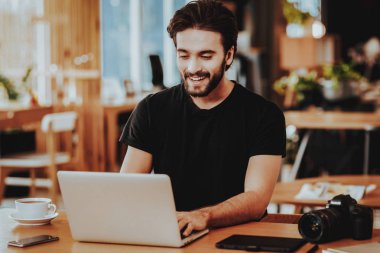 Dizüstü bilgisayarda çalışma Freelancer gülümseyen portresi. Yakışıklı beyaz Hipster grafik tasarımcı siyah T-Shirt oturur becerikli alet ile masada kapalı giyer. Mesafe iş ve Freelancing kavramı