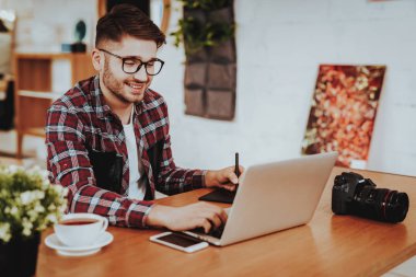 Dizüstü bilgisayarda çalışma Freelancer gülümseyen portresi. Yakışıklı beyaz Hipster grafik tasarımcı gözlük oturur masada kapalı Stylus kalem ile dijital Tablet kullanarak giyer. Mesafe iş kavramı