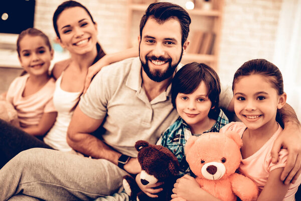 Portrait of Cute Smiling Family Sitting on Sofa. Smiling Parents with Children Sitting on Sofa at Home. Lovely Cheerful Family with Three Kids. Family Concept. Lifestyle Rest Relax Leisure Concept.