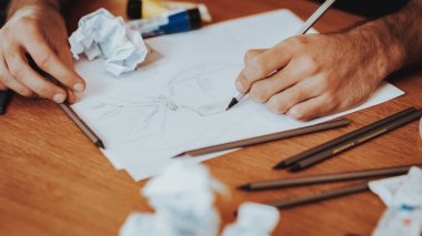 Sanatçı masaüstü kağıtları ve fırçalar ile closeup. Ahşap masa kalem çizim Holding erkek eller. Resim in masaüstü öğelerini, yalan. Yaratıcı sanat hobi ve sanatçı araçları kavramı