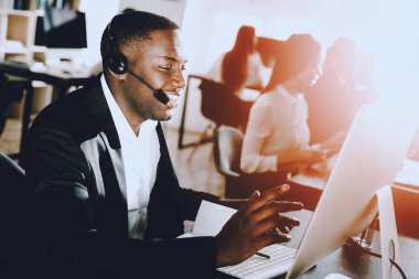 Çağrı merkezinde çalışan Afro Amerikalı adam oturuyor. Bilgisayar Yöneticisi. Çalışma alanı kişi. Danışman mikrofon ile. Müşteri hizmet anlayışı. Kulaklık kadında. Ofis operatör.