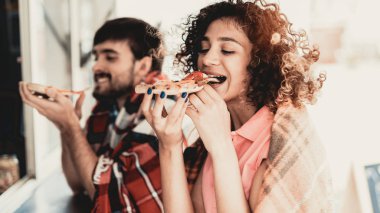 Genç çift damalı ekoseler Pizza yemek. Sokak gıda kavramı. Şehirde yiyecek. Abur cubur satış. Girfriend ve erkek arkadaşı. Yaz günü. Avrupa şehir meydanında. Battaniyeye gülümseyen insanlar.