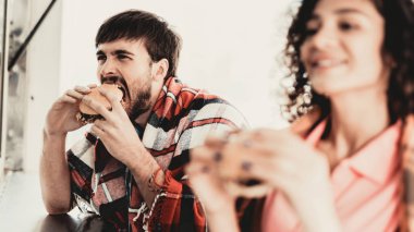 Damalı ekoseler hamburger yeme genç çift. Sokak gıda kavramı. Şehirde yiyecek. Abur cubur satış. Girfriend ve erkek arkadaşı. Yaz günü. Avrupa şehir meydanında. Battaniyeye gülümseyen insanlar.