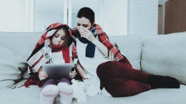 Damalı battaniye içinde kanepede oturan hasta aile. Anne ve kızı. Oda beyaz kanepe. Mutsuz kız. Hastalık kavramı. Sağlık ve sağlıklı yaşam konsepti. Peçeteler kullanarak. Dizüstü bilgisayar ile kız.