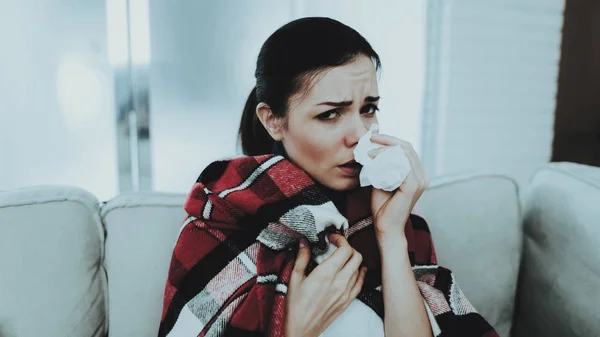 Woman with Cold on Sofa in Checkered Blanket. Girl at Home. Sick Young Woman. White Sofa in Room. Unhappy Woman. Disease Concept. Healthcare and Healthy Lifestyle Concept. Using Napkins.