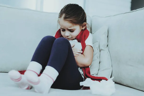 冷たい赤いスカーフのソファーに座っている少女 病気の少女 部屋で白いソファ 不幸な子 病気の概念 医療と健康的なライフ スタイルのコンセプトです 自宅の小さな女の子 — ストック写真