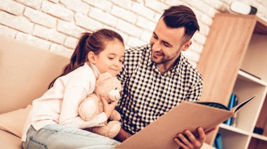 Elinde oyuncak ayı. Baba ve kızı kanepe. Birlikte vakit geçirmek. Babalar günü. Adam oyun kız ile. Beyaz iç. Adam kanepede kızla. Babası ile oynamak. Adam kitabı oku. Koltukta oturan.