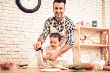 Evde yemek. Mutlu bir aile. Babalar günü. Kız ve erkek aşçı gıda. Adam ve çocuk masasında. Birlikte vakit geçirmek. Peynir rendeleyin. Rende elinde. Domates ve salatalık. Baba ve kızı birlikte.