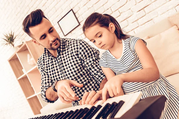 Man and Girl Play Piano. Play Piano Together. Father and Daughter on Sofa. Spend Time Together. Father\'s day. Man Play with Girl. White Interior. Girl wiht Man on Sofa. Play Piano and Sing.