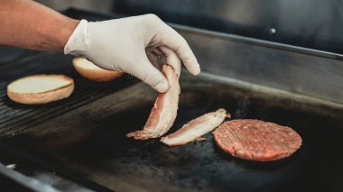 Yakın çekim. Yemek hamburger gıda kamyon işçisi. Sokak gıda kavramı. Şehirde yiyecek. Abur cubur satış. Sandviç hazırlanması. Sağlıksız yiyecek. Ellerinde eldiven. Lezzetli Hamburder. Lastik tarım eldivenler.