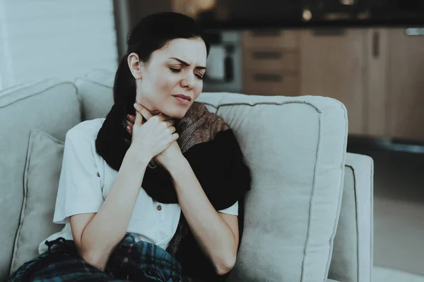 Upset Woman with Cold on Sofa in Scarf at Home. Sick Young Woman. White Sofa in Room. Unhappy Woman. Disease Concept. Healthcare and Healthy Lifestyle Concept. Unhappy Girl. Modern Medicine.