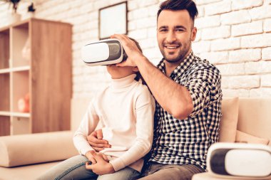 Joystick elinde. Sanal gerçeklik maskesi. Baba ve kızı. Birlikte vakit geçirmek. Babalar günü. Kızla oynayan adam. Video oyunu. Beyaz iç. Koltukta oturuyor. Kız maske sanal gerçeklik.