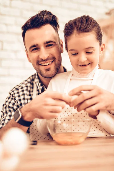 Cook Food at Home. Happy Family. Father\'s Day. Girl and Man Cook Food. Smiling Man and Child at Table. Spend Time Together. Knife in Hand. Tomatoes and Cucumber. Food on Table. Break Eggs into Bowl.