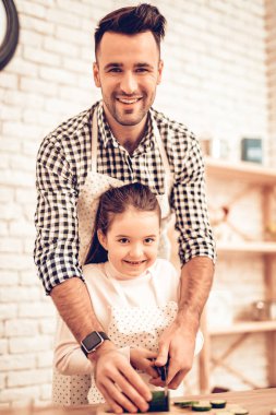 Evde yemek. Mutlu bir aile. Babalar günü. Kız ve erkek aşçı gıda. Adam ve çocuk masasında. Birlikte vakit geçirmek. Peynir rendeleyin. Rende elinde. Domates ve salatalık. Mutfak işlemi. En düşük RUB rendelenmiş.