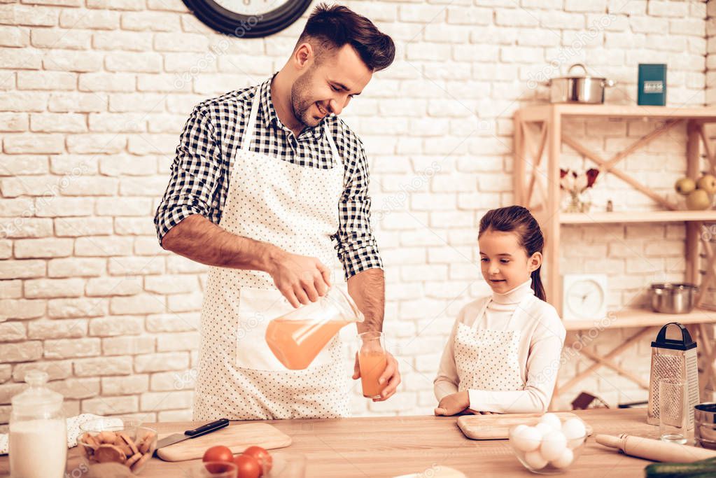Cook Food at Home. Father Feeds Daughter. Pour Juice in Glass. Happy Family. Father's Day. Girl and Man Cook Food. Man and Child at Table. Spend Time Together. Dad with Carafe in Hand. Family at Home.