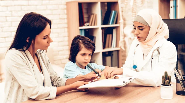 Mother Writing Medical Contract with Arabic Doctor. Confident Muslim Female Doctor. Child at the Pediatrician. Hospital Concept. Healthy Concept. Pediatrician Writes a Prescription.