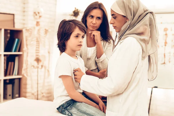 Arabic Female Doctor Examining a Little Boy. Child at the Pediatrician. Hospital Concept. Healthy Concept. Child Patient Visiting Doctor. Doctor Checking Heartbeat. ill Boy Lying on Bed near Mom.