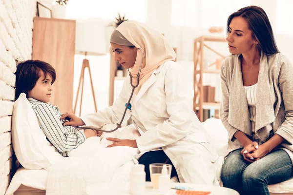 Arabic Female Doctor Examining a Little Boy. Child at the Pediatrician. Hospital Concept. Healthy Concept. Child Patient Visiting Doctor. Doctor Checking Heartbeat. ill Boy Lying on Bed near Mom.