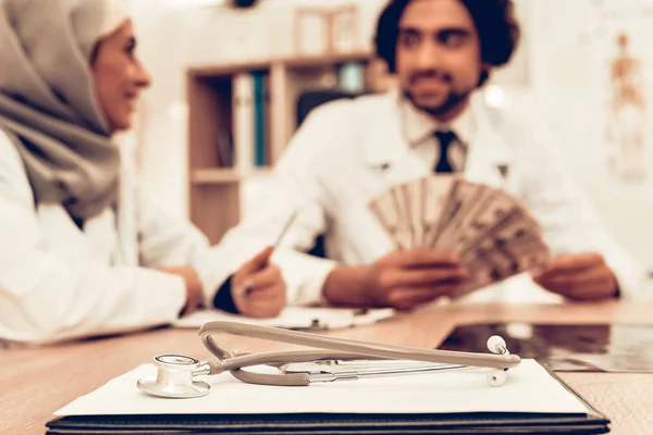 Arabic Doctors Counting Money After Work, Payday. Muslim Doctors Counting Dollars in Office. Arabic Doctors Holding Money, Medical Consultation. Hospital Concept.  Concept. Healthcare And Medicine.