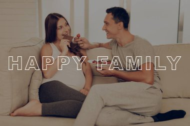 Kanepe üzerinde çocuklar yalan. Ebeveynler birbirine besleme. Göbek kız beklenti gebelik. Hamile kadın çikolata yiyin. Adam tutun çilek. Mutlu birlikte. Mutlu genç aile. Hamile Sit evde.