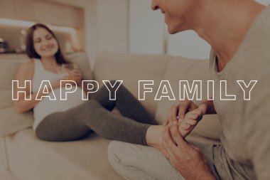 Adam hanımları ayak Kneads. Hamile kız mide ellerinde. Işık kanepe üzerinde hamile kadın yatıyor. Mutlu genç aile. Kadın mide. Göbek kız beklenti gebelik. Evde hamile Sit. Gülümsüyor anne.