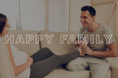 Işık kanepe üzerinde hamile kadın yatıyor. Mutlu genç aile. Adam hanımları ayak Kneads. Hamile kız mide ellerinde. Kadın mide. Göbek kız beklenti gebelik. Evde hamile Sit. Gülümsüyor anne.