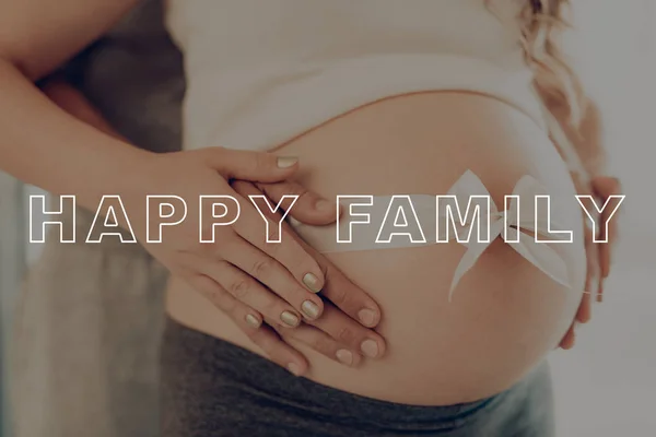 Close Up. Happy Young Family. White Bow on Stomach. Husband Hugs. Hands on Pregnant Girl Stomach. Woman Bare Stomach. Belly Girl Anticipation Pregnancy. Preggers Sit at Home. Smiles Parents.