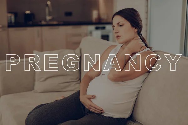 Pregnant Woman Stiff Neck. Parturient Girl Clings to Stomach. Daily Life Expectant Mother. Expectant Mother Get Well. Preggers Sit at Home. Pregnant Female on Light Sofa. Frown Pregnant Woman.
