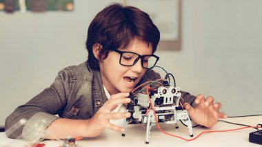 Masada oturan ve evde Robot inşa çocuk. Genç çocuk gömlek. Kapalı sevinç. Modern hobi kavramı. Modern teknoloji. Robot mühendislik kavramı. Genç Robor ile. Eğlenmek için yenilik.