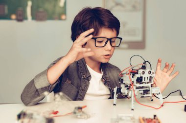 Masada oturan ve evde Robot inşa çocuk. Genç çocuk gömlek. Kapalı sevinç. Modern hobi kavramı. Modern teknoloji. Robot mühendislik kavramı. Genç Robor ile. Eğlenmek için yenilik.