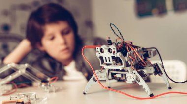 Masada oturan ve evde Robot inşa çocuk. Genç çocuk gömlek. Kapalı sevinç. Modern hobi kavramı. Modern teknoloji. Robot mühendislik kavramı. Genç Robor ile. Eğlenmek için yenilik.