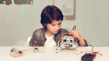 Masada oturan ve evde Robot inşa çocuk. Genç çocuk gömlek. Kapalı sevinç. Modern hobi kavramı. Modern teknoloji. Robot mühendislik kavramı. Genç Robor ile. Eğlenmek için yenilik.
