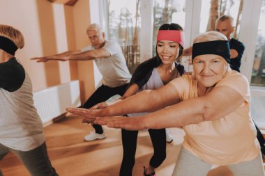 Etkin emekli. Hasta giyen üniforma spor gülümseyen. Genç eğitmen gösteri Exerscises. Grup yaşlı insanlar meşgul. Bakım evi. Tedavi jimnastiği. Sağlık yaşam tarzı yaşlı insanlar.
