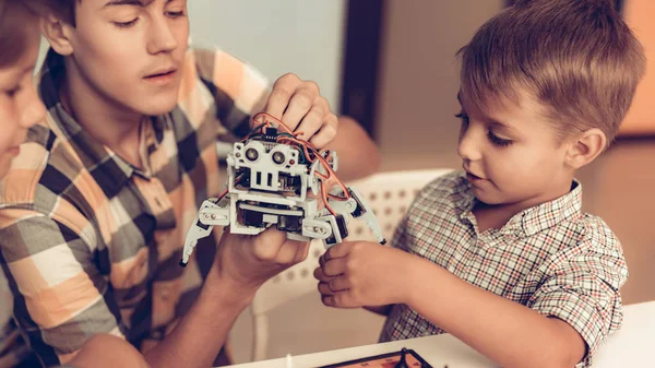 Teenager Demonstrating Robot to Two Sitting Boys. Young Boy in Shirt. Indoor Joy. Modern Hobby Concept. Modern Technology. Robot Engineering Concept. Teenager with Robor. Innovation for Fun.