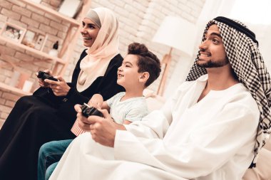 Konsolda evde oynarken mutlu Arap aile. Koltukta oturan aile. Dijital aygıt kullanan adam. Evde Boay gülümseyerek. Müslüman aile. Boy gülümseyerek. Genç Arap kadın. Siyah elbiseli kadın.