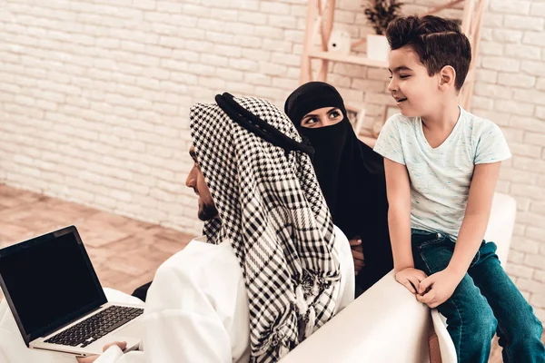 Young Arabic Family Using Laptop on Sofa at Home. Family Sitting on Sofa. Man Using Digital Device. Smiling Boay at Home. Muslim Family. Smiling Boy. Young Arabian Woman. Woman in Black Veil.