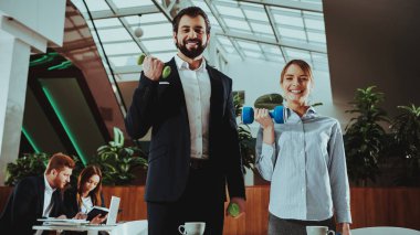 Kurumsal spor yaşam tarzı. Sağlık iş adamları. Ofis çalışanları dumbell ile çalışma. İşçiler Fitness egzersizleri yapıyor. Yoga pratik. Gülümseyen için sağlıklı kadın çalışan adam.