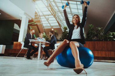 Kurumsal spor yaşam tarzı. Sağlık iş adamları. İşçi ofiste rahat ol. Yoga pratik. Mutlu ofis müdürü. Kadın topu Dumbbells ile dengede. Çalışmalarına uzanan kız.